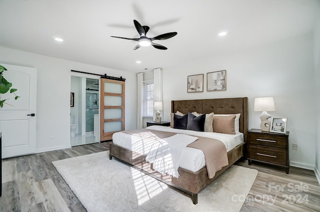 bedroom with a barn door, ceiling fan, ensuite bath, and light hardwood / wood-style floors