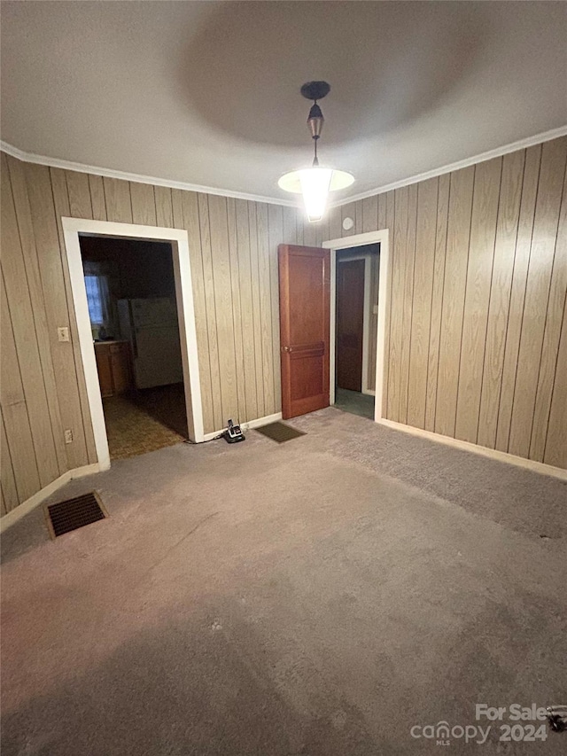 carpeted empty room featuring crown molding and wooden walls