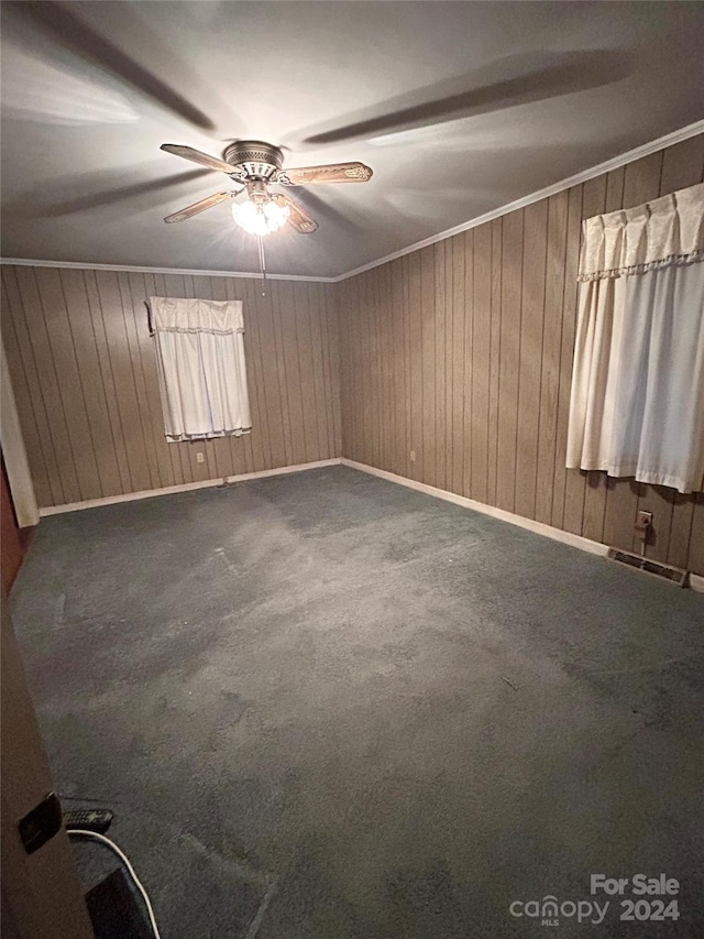 spare room with carpet flooring, ceiling fan, wood walls, and crown molding