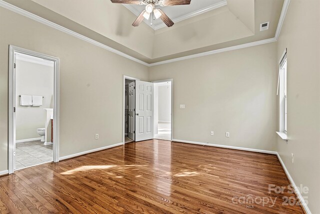 unfurnished bedroom with wood-type flooring, ornamental molding, ensuite bathroom, and a tray ceiling