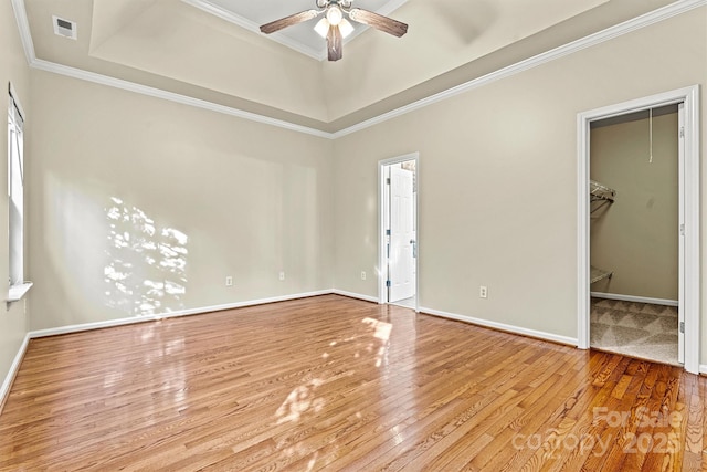 unfurnished bedroom featuring crown molding, a walk in closet, light hardwood / wood-style floors, and a raised ceiling