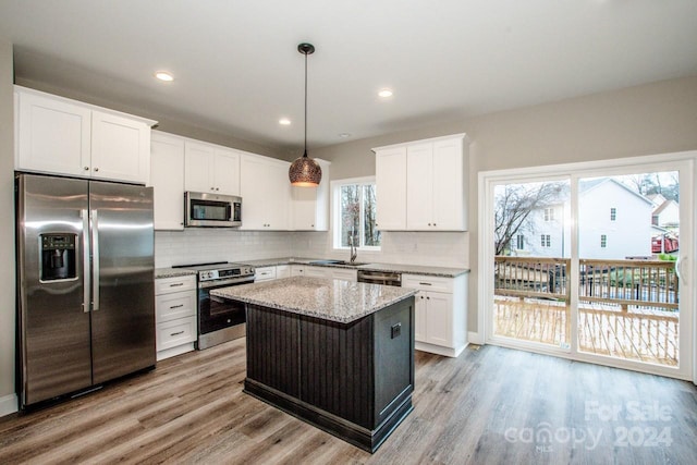 kitchen with appliances with stainless steel finishes, tasteful backsplash, decorative light fixtures, light hardwood / wood-style floors, and a kitchen island