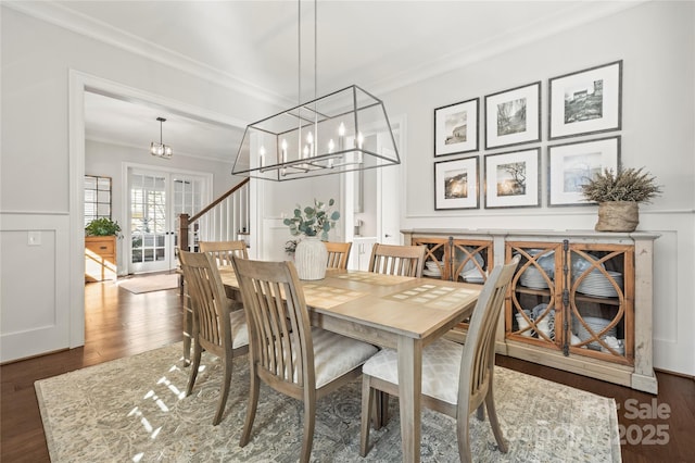 dining space featuring french doors, crown molding, a decorative wall, wood finished floors, and a chandelier