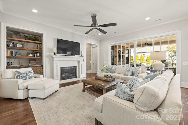 living area with dark wood finished floors, a ceiling fan, a glass covered fireplace, crown molding, and recessed lighting