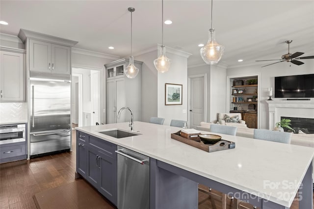 kitchen featuring dark wood finished floors, appliances with stainless steel finishes, open floor plan, crown molding, and a sink