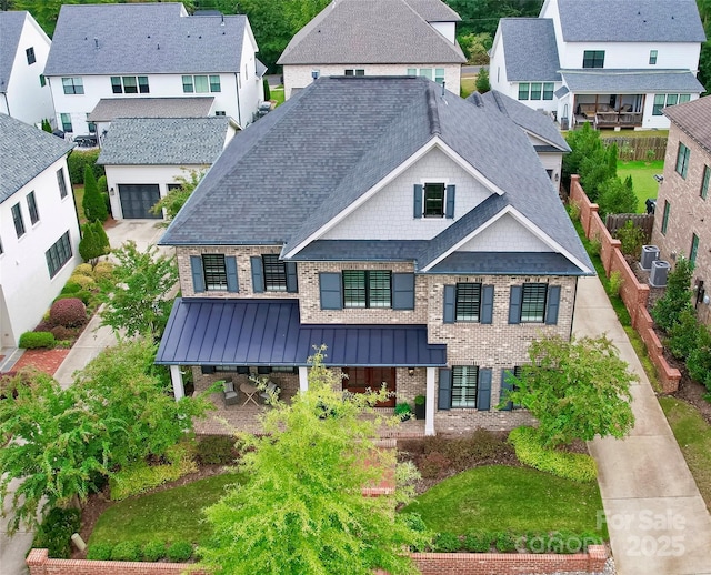 view of front of property featuring a shingled roof, metal roof, a standing seam roof, fence, and brick siding