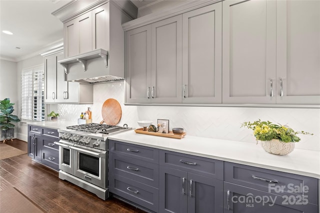 kitchen with light countertops, ornamental molding, wall chimney range hood, double oven range, and dark wood finished floors