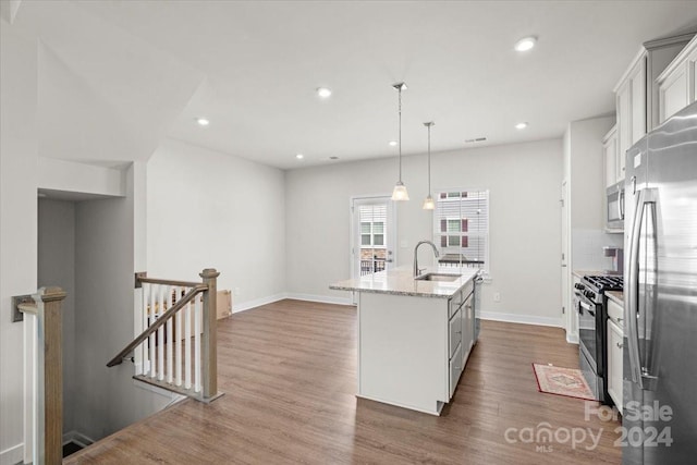 kitchen featuring stainless steel appliances, sink, decorative light fixtures, white cabinetry, and an island with sink