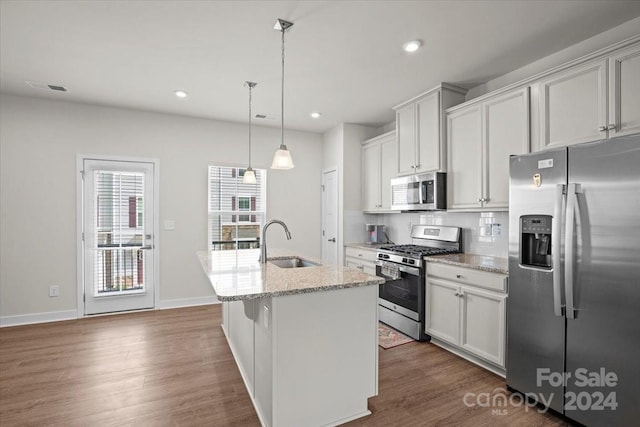 kitchen with appliances with stainless steel finishes, dark hardwood / wood-style flooring, sink, a center island with sink, and hanging light fixtures