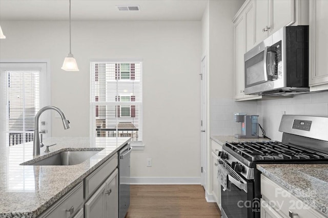 kitchen with sink, light stone counters, hardwood / wood-style floors, decorative light fixtures, and appliances with stainless steel finishes