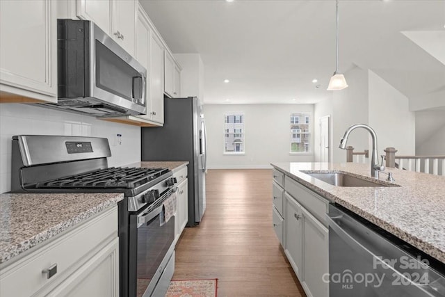 kitchen with stainless steel appliances, sink, light hardwood / wood-style floors, white cabinetry, and hanging light fixtures