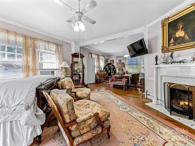 living room featuring hardwood / wood-style floors, ceiling fan, crown molding, and a brick fireplace