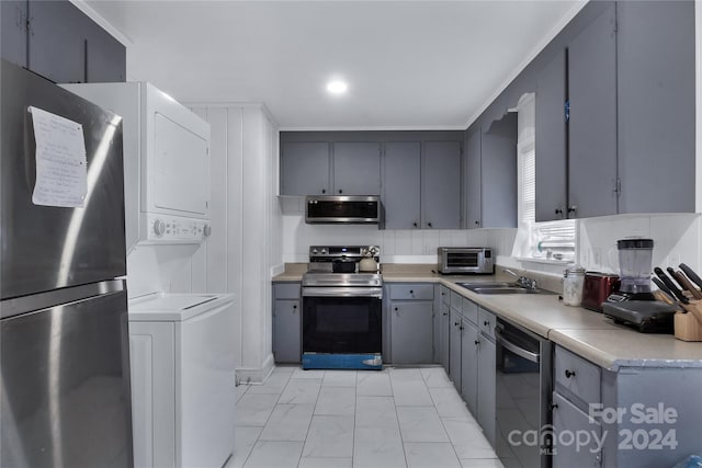 kitchen with gray cabinets, stacked washing maching and dryer, sink, and stainless steel appliances