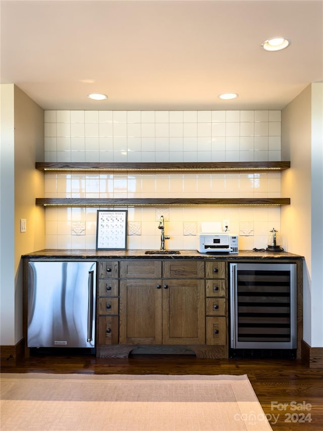 bar featuring beverage cooler, sink, decorative backsplash, dark hardwood / wood-style flooring, and stainless steel refrigerator