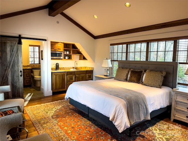 bedroom featuring sink, dark wood-type flooring, a barn door, vaulted ceiling with beams, and ensuite bathroom