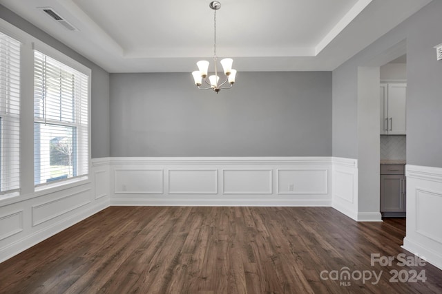 spare room featuring a notable chandelier, a raised ceiling, and dark wood-type flooring