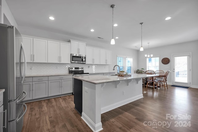 kitchen featuring light stone countertops, stainless steel appliances, dark hardwood / wood-style flooring, an island with sink, and pendant lighting