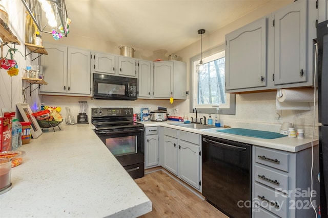 kitchen featuring sink, black appliances, gray cabinets, light hardwood / wood-style floors, and hanging light fixtures