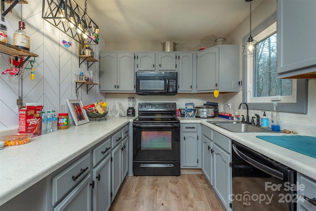 kitchen with black appliances, sink, gray cabinets, light wood-type flooring, and decorative light fixtures