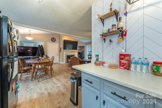 kitchen with pendant lighting, light hardwood / wood-style floors, black fridge, and blue cabinetry