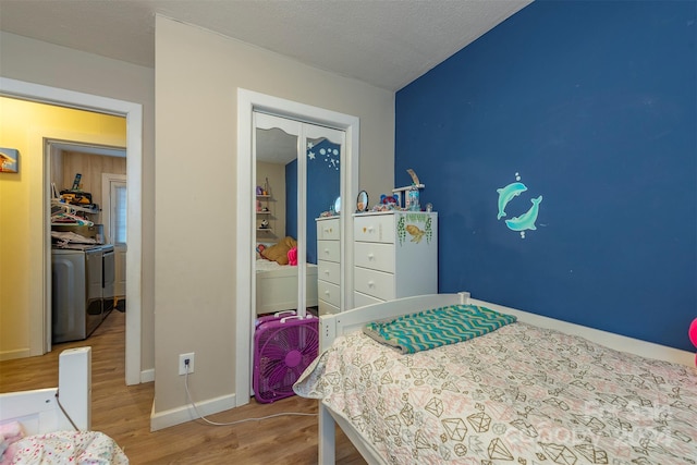 bedroom featuring washing machine and clothes dryer, hardwood / wood-style floors, vaulted ceiling, a textured ceiling, and a closet