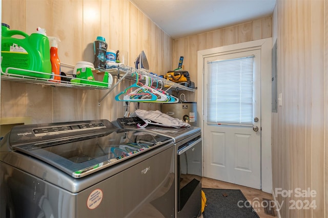 clothes washing area featuring electric water heater, wood walls, independent washer and dryer, and hardwood / wood-style flooring