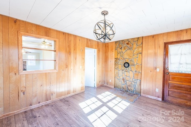 unfurnished dining area with wood walls, light hardwood / wood-style flooring, and ceiling fan with notable chandelier