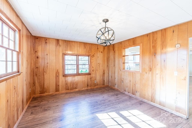 spare room featuring wooden walls, wood-type flooring, and an inviting chandelier