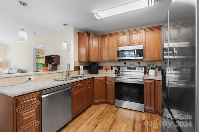 kitchen featuring sink, hanging light fixtures, stainless steel appliances, light stone counters, and light hardwood / wood-style flooring