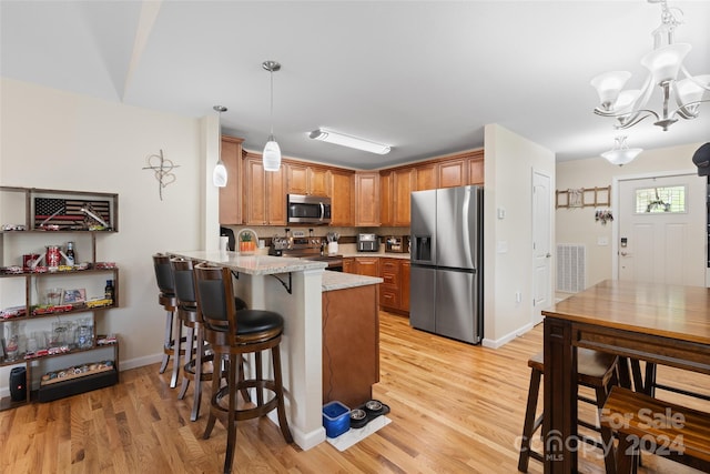 kitchen with decorative light fixtures, kitchen peninsula, stainless steel appliances, and light hardwood / wood-style flooring