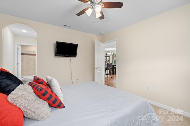 carpeted bedroom featuring ceiling fan with notable chandelier and ensuite bathroom