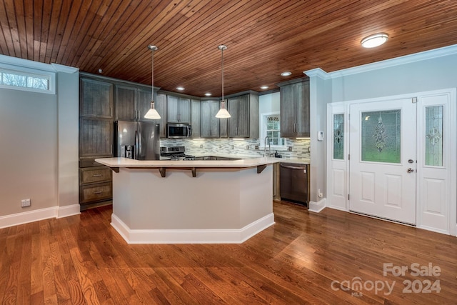 kitchen with dark wood-type flooring, hanging light fixtures, crown molding, appliances with stainless steel finishes, and a kitchen island