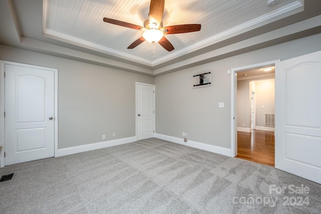 unfurnished bedroom with ceiling fan, wooden ceiling, carpet floors, a tray ceiling, and ornamental molding