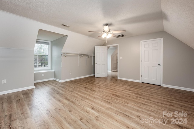 additional living space with a textured ceiling, ceiling fan, light hardwood / wood-style floors, and lofted ceiling