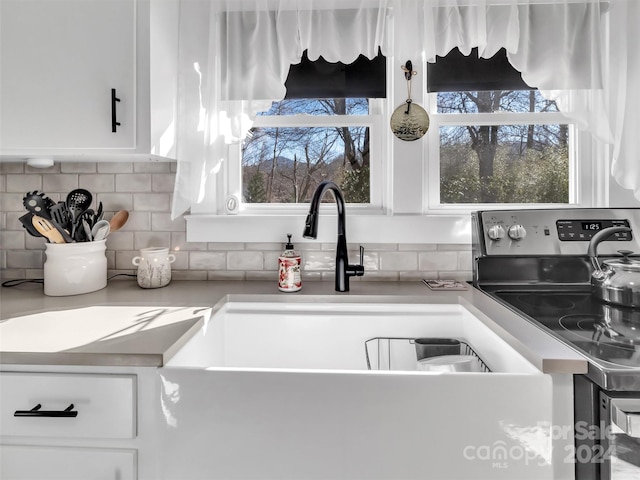 kitchen with electric range, white cabinetry, and backsplash