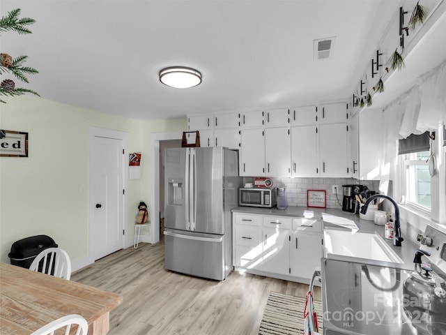 kitchen featuring tasteful backsplash, white cabinets, stainless steel appliances, and light wood-type flooring