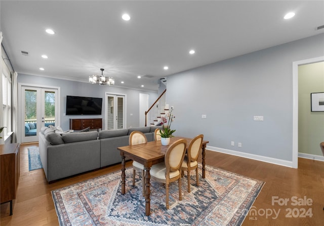 dining space with hardwood / wood-style flooring, french doors, ornamental molding, and an inviting chandelier