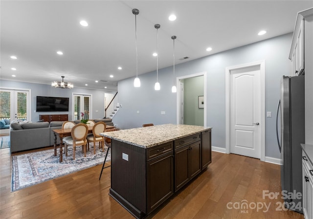 kitchen with stainless steel refrigerator, dark brown cabinetry, hanging light fixtures, dark hardwood / wood-style floors, and a kitchen bar