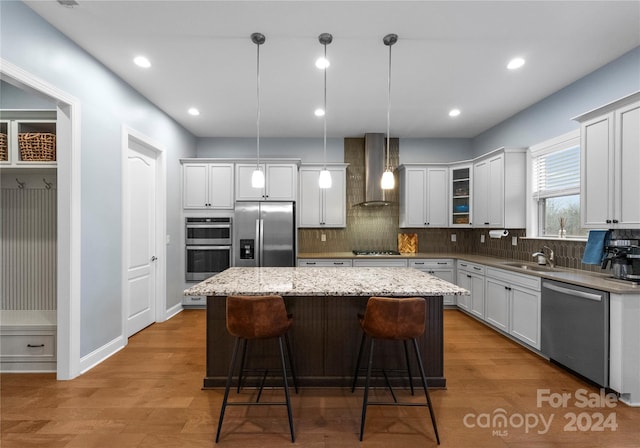 kitchen featuring a center island, wall chimney range hood, pendant lighting, appliances with stainless steel finishes, and hardwood / wood-style flooring