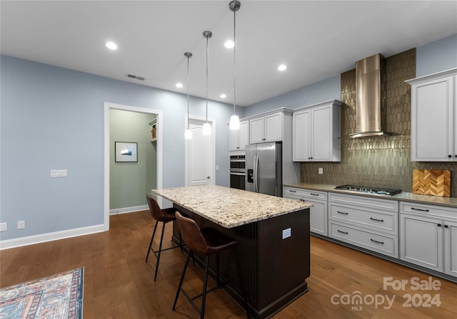 kitchen with wall chimney range hood, dark hardwood / wood-style flooring, a breakfast bar area, a kitchen island, and appliances with stainless steel finishes