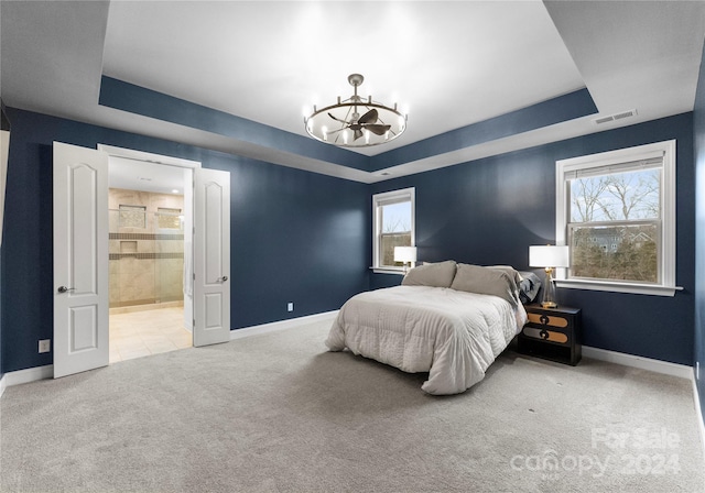 bedroom featuring carpet flooring, ensuite bathroom, a tray ceiling, and a notable chandelier