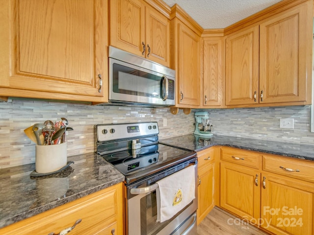 kitchen with dark stone counters, light hardwood / wood-style flooring, decorative backsplash, a textured ceiling, and appliances with stainless steel finishes