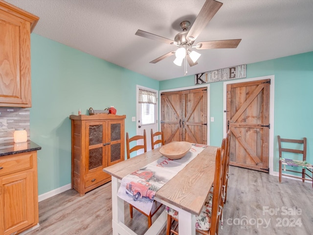 dining room with a barn door, ceiling fan, light hardwood / wood-style flooring, and a textured ceiling