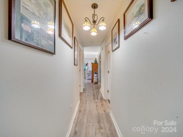 corridor with light hardwood / wood-style floors and a notable chandelier