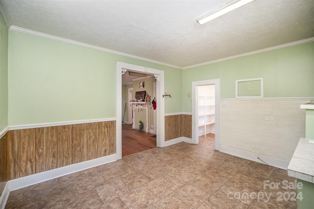 empty room with a textured ceiling, wooden walls, and ornamental molding