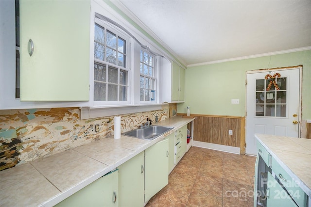 kitchen with tile countertops, crown molding, wood walls, and sink