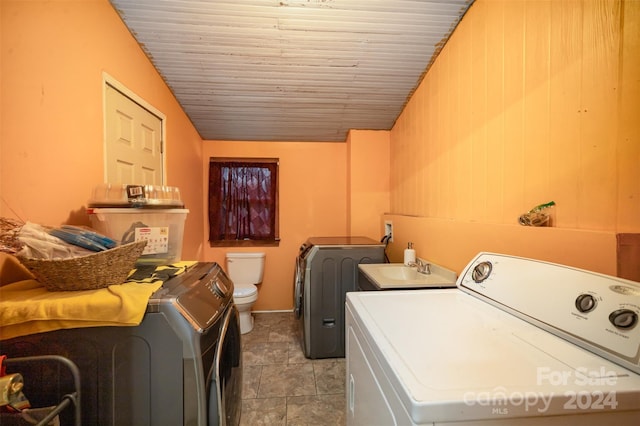 laundry area featuring wood walls, sink, light tile patterned floors, and independent washer and dryer