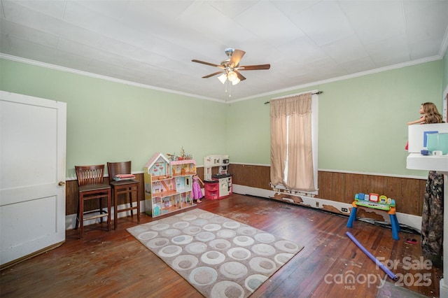 game room with dark wood-type flooring, ornamental molding, ceiling fan, and wood walls