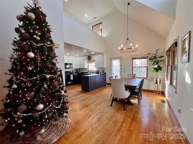 dining area with an inviting chandelier, high vaulted ceiling, and light hardwood / wood-style flooring