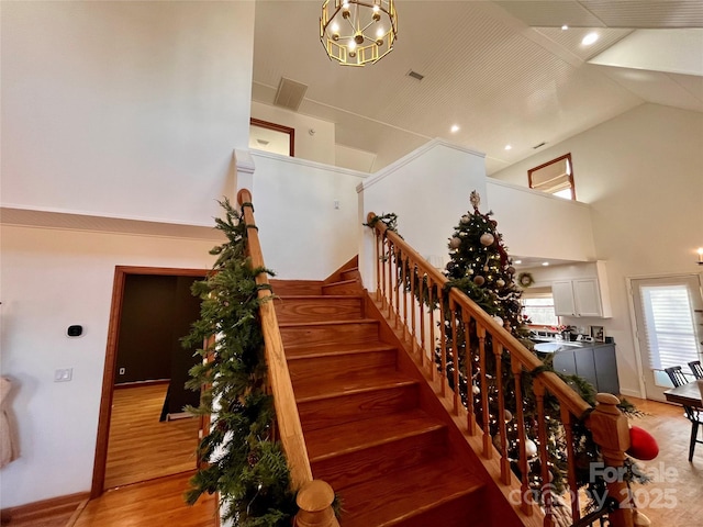 stairs featuring hardwood / wood-style floors, high vaulted ceiling, and a chandelier